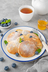 Delicious homemade pancakes with blueberries and honey, sprinkled with powdered sugar on top on a gray concrete background.