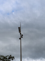 Tall, modern spotlight pole with multiple fixtures pointing down, against a dramatic overcast sky