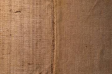 Close-up of natural brown burlap or jute sackcloth texture with a vertical stitched seam down the middle. Rustic textile background, ideal for packaging, organic, and craft concepts