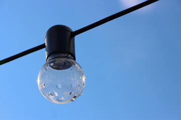 Single string light bulb against a blue sky just after rainfall.