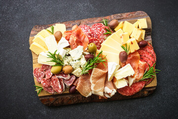 Italian appetizers. Cheese and meat - jamon, salami with olives at wooden serving board at black...