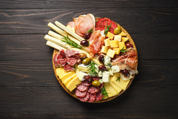 Antipasto at wooden serving board. Cheese and meat - jamon, salami with olives at wooden table. Top view with copy space.