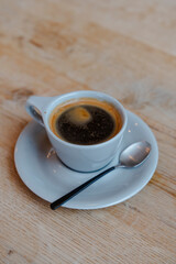 Close-up of a cup of black coffee with a spoon on a wooden table top.