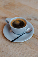 Elegant cup of coffee, dark and rich, on a wooden table, beside a spoon.