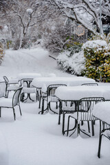 A snowy day scene with tables and chairs covered in thick, fresh snowfall.