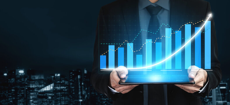 A businessman in formal attire holds a tablet displaying a vibrant digital growth chart against a dark urban background, symbolizing financial success. Impute