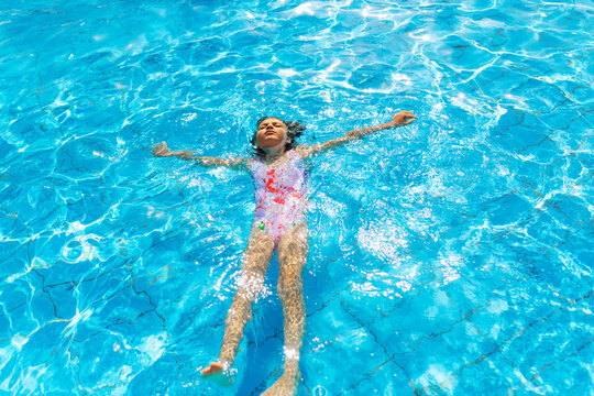 Portrait of resting 7 years old girl floating on his back in swimming pool on sunny day - Powered by Adobe