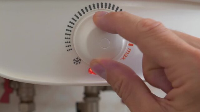 Regulator for heating cold water in boiler. Man turns temperature control on heater of water. Red light indicator comes off, boiler has turned off