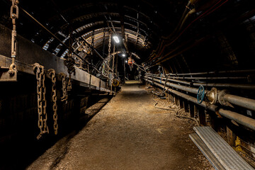 Deep underground, a long mining tunnel stretches into darkness as massive coal-cutting machines...