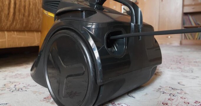 Man pulls an electrical cord out of vacuum cleaner. Vacuum cleaner cord retractor or vacuum cleaner cord winding mechanism. Mechanism or system for winding cord in vacuum cleaner