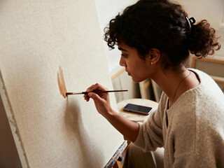 Woman creating a cozy atmosphere while painting a canvas in a warm, inviting home space