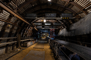 Underground coal mining scene with massive industrial machines operating inside long tunnels and narrow galleries. Dim light, heavy equipment, and rough walls show the harsh conditions of subterranean