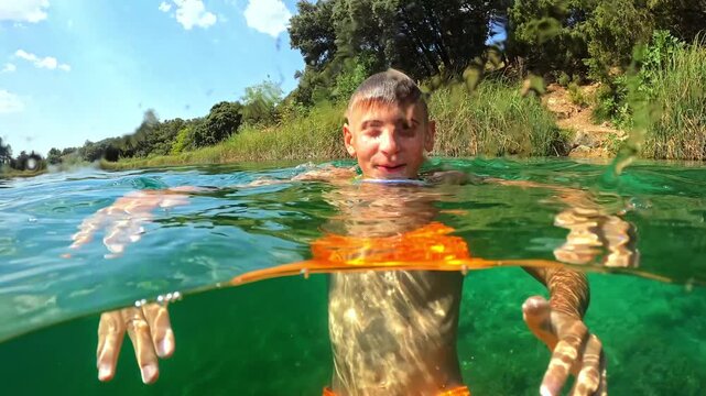 Happy boy with swimming goggles enjoy sunny day, diving from surface into clear green water of lake during summer vacation, creating beautiful split-level view