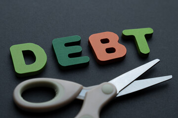 Letters spelling “DEBT” with a pair of scissors. Cutting debt, financial freedom, savings, and money management concept.