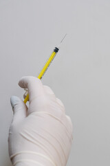 A gloved medical professional&rsquo;s hand holding a syringe against a white background. Concept A sterile tool prepared for clinical use.