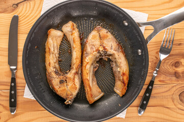 Two fried carp steaks on a frying pan, top view, macro