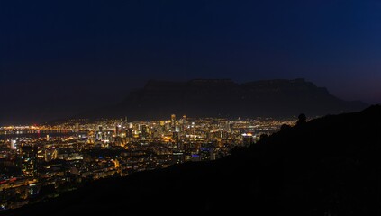 Fototapeta premium Night view of a cityscape with illuminated buildings and a mountain backdrop, urban density, tourism