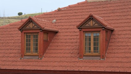 Fototapeta premium The roof of a red house featuring detailed window architecture, rustic design, outdoor setting, seasonal change