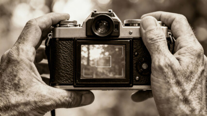 Elderly hands hold vintage camera, focus on viewfinder, capturing a moment, sepia tones highlight timeless photography art
