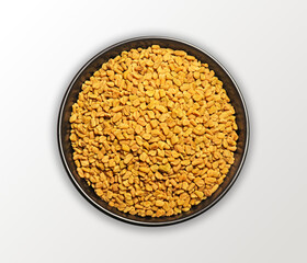 A clean top-view photograph of fenugreek seeds arranged in a black round bowl on a minimal white background. The shot captures the natural texture, earthy tones, and organic shapes of methi seeds.