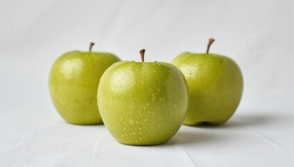 Three green apples on a white surface, beneficial fiber-rich choice