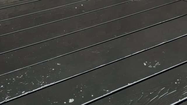 Closeup of water being thrown over some stain mess on the flat surface of outside composite decking boards, followed by a broom sweeping the excess water away.