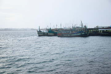 Fishing boats docked at a harbor with calm ocean water under a cloudy sky showing a candid local daily life in the island of Koh Sdach, Cambodia