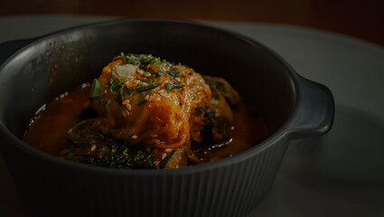 Close up to braised pork stew wrapped in kimchi called kimchi jjim served in a ceramic bowl, authentic traditional Korean food