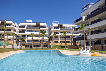 Luxury apartment buildings with pool, palm trees, and inflatable swan under blue sky