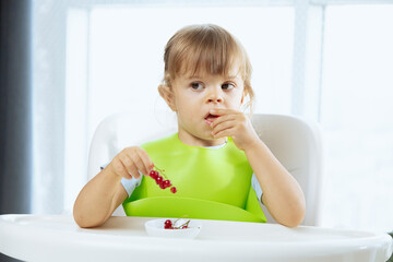 Funny baby girl eating red berries, red currants. Healthy snack for children, fruits as a source of vitamins