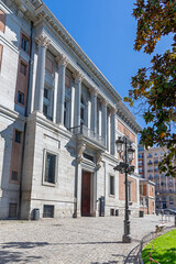 El Prado Museum on a sunny spring morning, showcasing elegant neoclassical architecture, grand statues, and lush green trees framing its bright, inviting façade with added charm