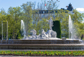 Close-up of Madrid’s Fuente de Neptuno, showing the white marble Neptune with trident, surrounded by horses and a strong water jet, all framed by vibrant green trees