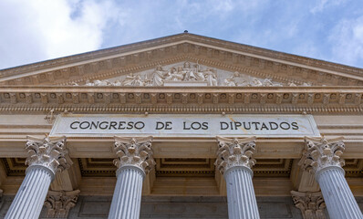 The neoclassical facade of the Spanish Congress of Deputies features six columns, a pediment, steps, and two large bronze lion statues flanking the main golden doorway