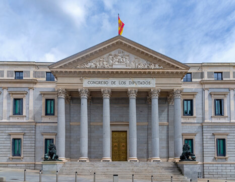 The neoclassical facade of the Spanish Congress of Deputies features six columns, a pediment, steps, and two large bronze lion statues flanking the main golden doorway