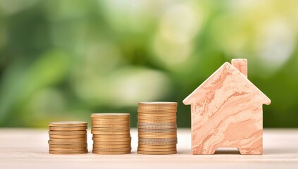 Stack of coins, pink piggy bank and wooden house on blurred green garden backdrop, financial planning and saving strategy