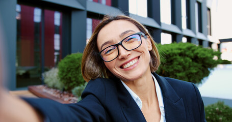 POV business woman having on video call using a smartphone while sitting near an modern building. Smiling mature woman in a formal suit has online conversation with a client or business partner