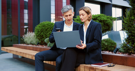 Senior entrepreneurs at a business meeting in an outdoor restaurant are discussing a project on a laptop. Male and female talking and typing on keyboard. Man and woman having work discussion.