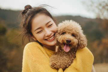 屋外で愛犬のトイプードルを抱きしめ笑顔を見せるアジアの若い女性 / Young Asian woman smiling while hugging her pet Toy Poodle outdoors