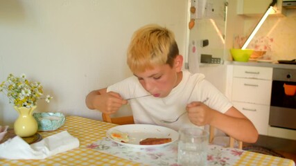 white boy trying dinner quietly at kitchen table, spoon and bowl closeup, floral vase by plate, focused small