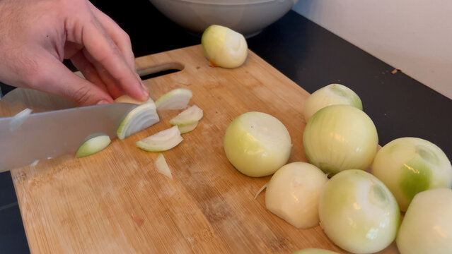 Chef hand swiftly slicing onions on rustic wooden cutting board.