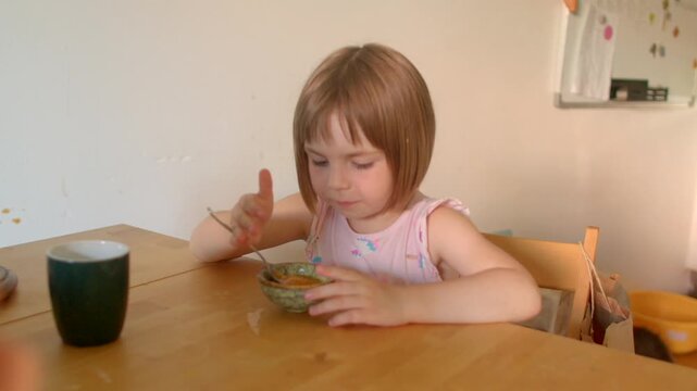 caucasian girl hesitating to eat cereal at wooden table, spoon held slowly, thoughtful refusal, minimalistic