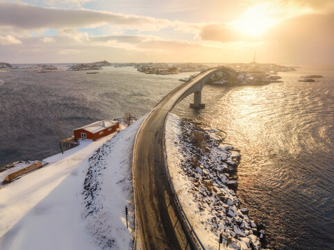 Aerial winter view of coastal bridge in Lofoten islands, Norway, with snow-covered shoreline, Arctic water, and soft sunset light. Top drone view of road, houses, rorbu, and islands. Nordic landscape - Powered by Adobe