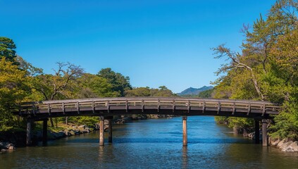 Fototapeta premium Wooden bridge spanning a river under a clear blue sky, showcasing natural beauty and tranquility