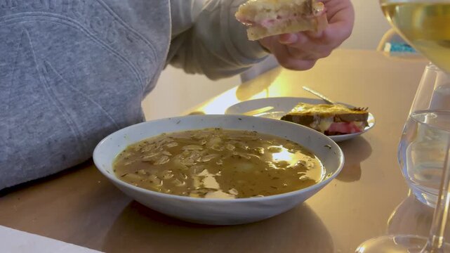 Hand dipping cheese sandwich piece into hot savory soup broth
