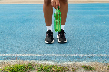 Athlete standing on a blue running track, holding a green water bottle for hydration