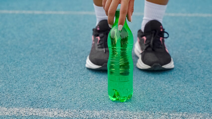 Athlete's hand holding a green water bottle, staying hydrated during sports on a blue track