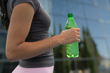 Woman hydrating with a green bottle of water after exercising in an urban environment