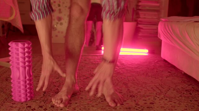 caucasian man performing toe touch stretch near foam roller and neon lamp, flexible movement and hamstring