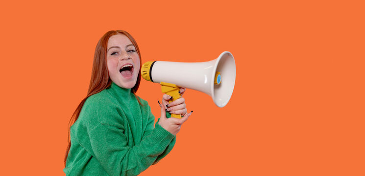 Young woman enthusiastically using a megaphone against a bright orange backdrop