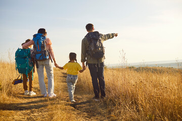 Family hiking with backpack on nature trail. Parents guide children along a sunlit path as dad points to the horizon, enjoying outdoors and travel together. Concept family unity and adventure.